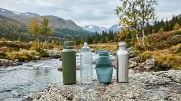 Fyra vattenflaskor i olika material uppradade på en klipphäll vid en fjällbäck